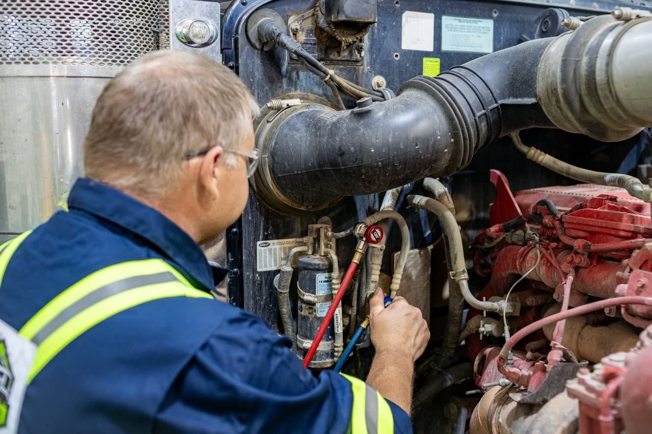 General Diesel Repair Maintenance worker in a high‑visibility vest inspects hoses and gauges on a large diesel engine of a truckemergency?